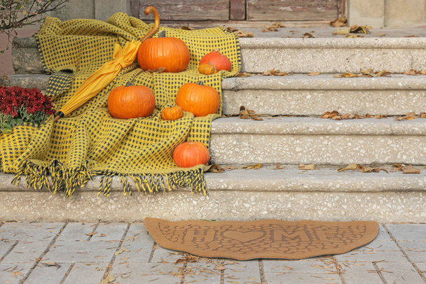 Doormat with plaid, pumpkins and umbrella near entrance of house on autumn day - Photo, Image