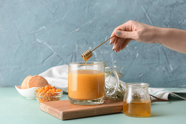 Жінка додає мед до здорового обліпихового чаю в чашку
 - Фото, зображення