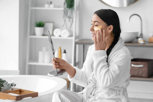 Beautiful Asian woman applying under-eye patches in bathroom - 写真・画像