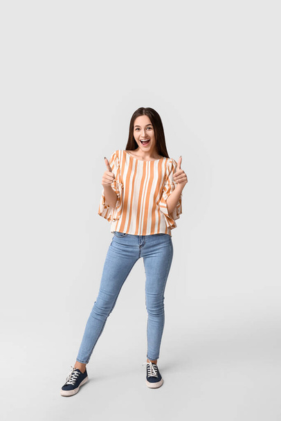Beautiful young woman showing thumbs-up on light background - Photo, Image