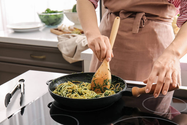 Kobieta gotowanie smaczny makaron ze szpinakiem w kuchni - Zdjęcie, obraz
