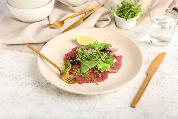 Plate with tasty veal carpaccio, glass of water and fresh sprouts on light background - Foto, immagini