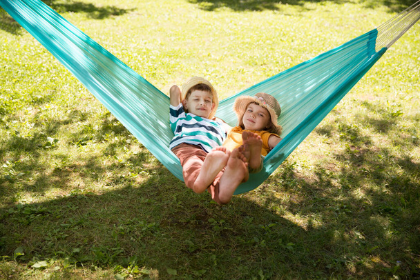 Two kids swing in a hammock in a summer park or garden. - Zdjęcie, obraz