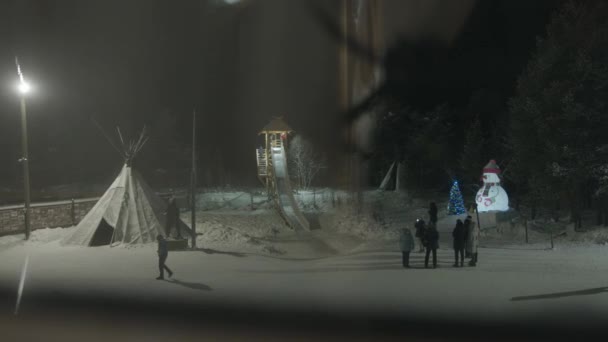 Un groupe de touristes inspecte une aire de jeux décorée pour Noël et se promène à partir d'une soirée d'hiver glissante en bois - Séquence, vidéo