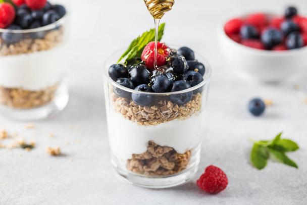 Honey is poured on granola with yogurt, blueberries and raspberries. Healthy breakfast. Menu, recipe. - Photo, image