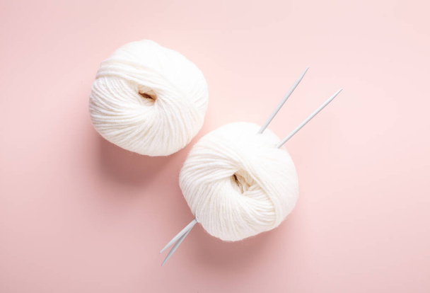 White knitting wool and knitting needles on pastel pink background. Hobby knitting. Top view - Фото, изображение