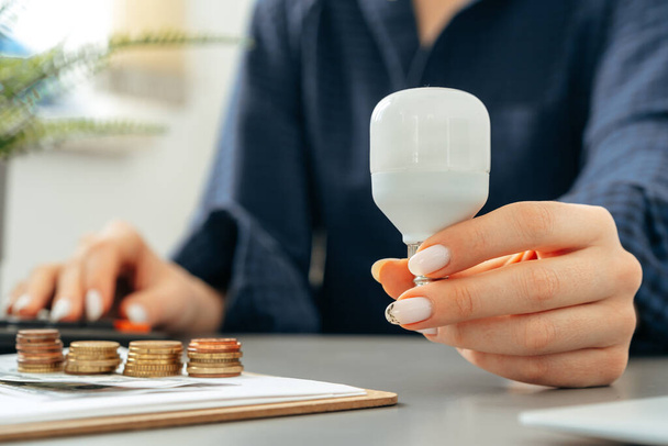 Female hand holding a light bulb above the table - Fotografie, Obrázek
