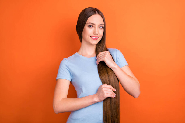 Photo of optimistic long hairdo young lady touch hair wear blue t-shirt isolated on vivid orange color background - Foto, immagini