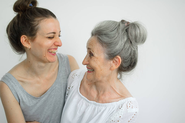 Glückliche Seniorin umarmt ihre erwachsene Tochter, die Frauen lachen zusammen, aufrichtige Familie unterschiedlichen Alters hat Spaß auf weißem Hintergrund, Muttertag. - Foto, Bild