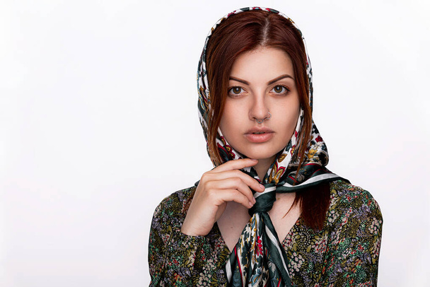 Portret van een jonge vrouw met een doorboorde neus en een modieuze hoofddoek. Witte achtergrond, ruimte voor tekst. Schoonheid, mode concept. - Foto, afbeelding