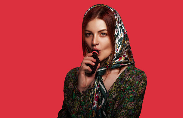Egy nő, aki elektromos cigarettát szív kilyukasztott orral és divatos fejkendővel. Piros háttér, hely a szövegnek. Szépség, divat koncepció. - Fotó, kép