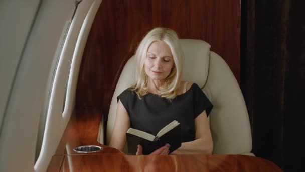 Hermosa mujer rica madura leyendo libro o portátil mientras vuela en avión privado. Lujo viajando en jet privado. - Imágenes, Vídeo