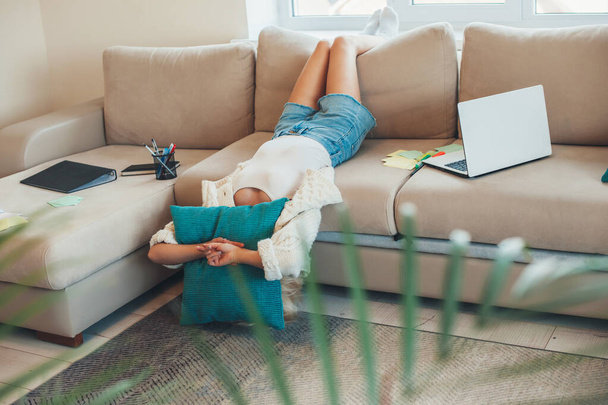 Mulher caucasiana cansada está deitada em um sofá enquanto faz lição de casa usando um laptop - Foto, Imagem