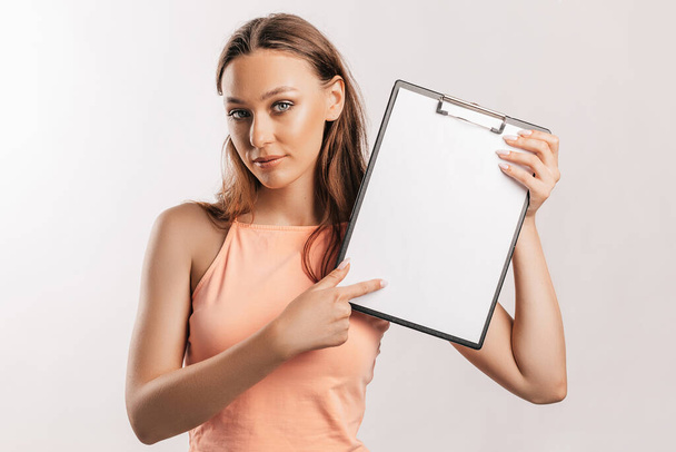 Girl student points to the sheet. Beautiful young business woman holds a clipboard with mockup blank space isolated on gray background. Study and business concept. Online learning cover - Foto, Imagem