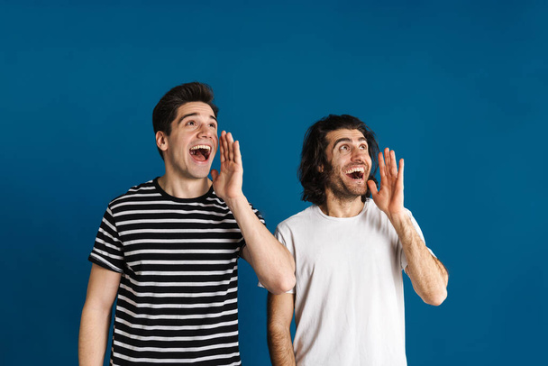 White excited two men gesturing and screaming aside isolated over blue background - Foto, Imagen