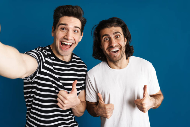 White excited two men gesturing thumbs up while taking selfie photo isolated over blue background - Zdjęcie, obraz