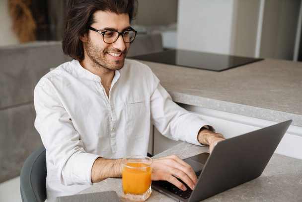 Smiling mid aged brunette turkish man sitting at the table with laptop computer at home - 写真・画像