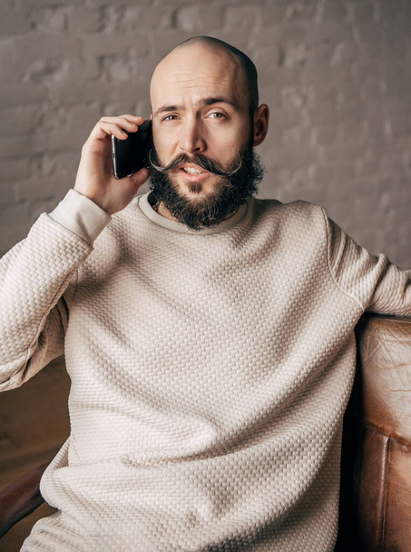 un joven calvo blanco con barba está hablando por teléfono en la habitación - Foto, imagen
