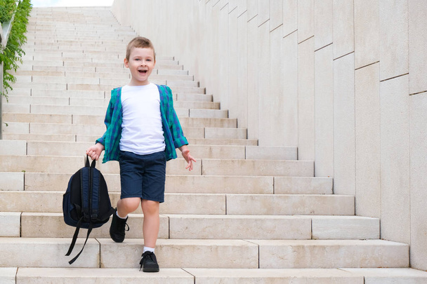 Un écolier avec un sac à dos à la main sur le chemin de l'école descend les escaliers. Retour à l'école. - Photo, image