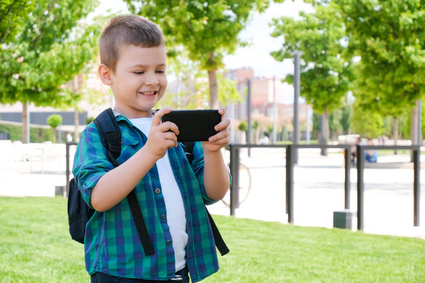 Happy schoolboy looking at smartphone screen and smiling, video call, online games on smart phone - Fotografie, Obrázek