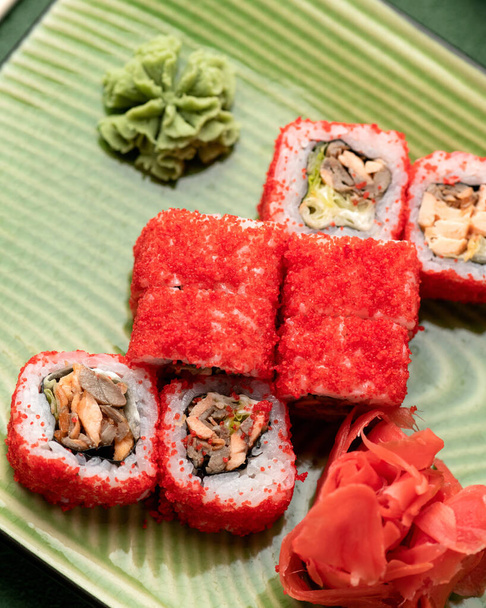 Red California Sushi roll in masago or tobiko caviar. Inside-out Japanese Sushi Set on green background. Bright colors. Healthy Oriental food. Soft focus. Vertical format. Closeup shot - Photo, Image