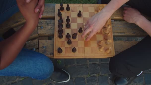 Два студента играют в шахматы, сидя на скамейке на закате - Кадры, видео
