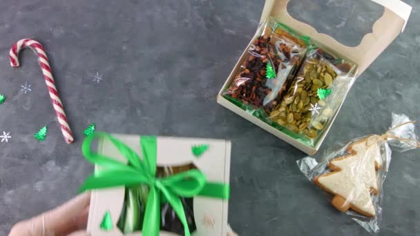 Chica envuelve caja de regalo con frutos secos conjunto envuelto individualmente. Alimentación saludable. Celebración navideña vacaciones preparando eco snack natural en manos femeninas.Consumo consciente dulces caseros - Imágenes, Vídeo