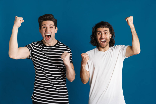 White excited two men exclaiming and making winner gesture isolated over blue background - Foto, afbeelding