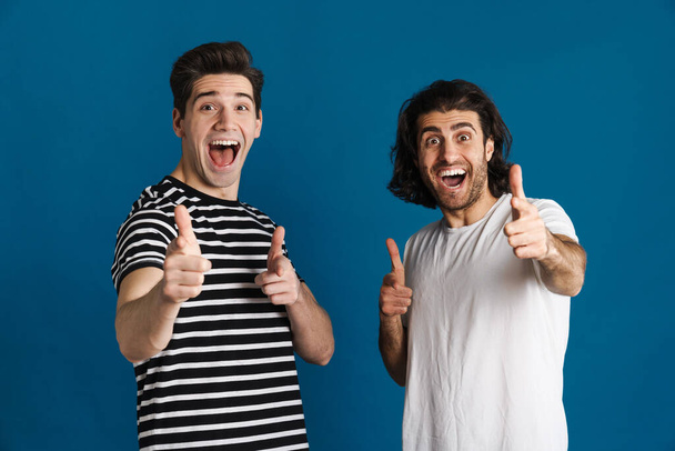 White excited two men exclaiming and pointing finger at camera isolated over blue background - Zdjęcie, obraz