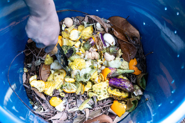 Das Mischen der grünen und braunen Materialien von Hand im Kompostbehälter - Foto, Bild