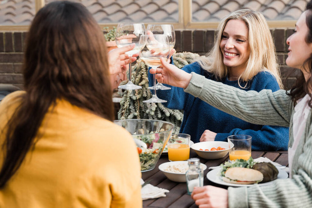 Junge multiethnische Menschen jubeln mit Wein und essen im Freien im Terrassenrestaurant - Frauengesicht in der Mitte im Fokus - Foto, Bild