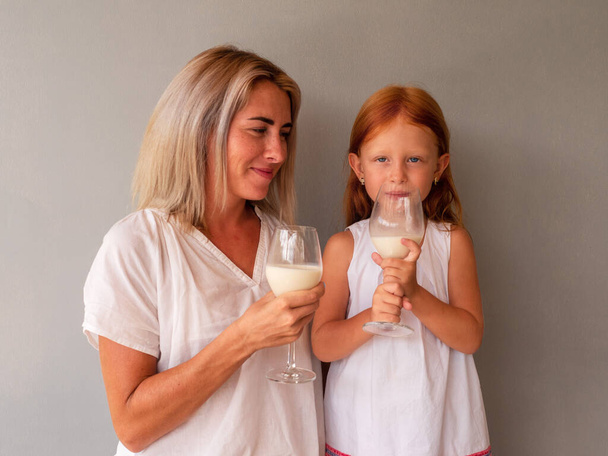 Mom and red-haired daughter drink milk at the table from glasses - Foto, Bild