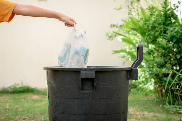 Χέρι του ανθρώπου ρίχνουν σκουπίδια σε πλαστικές σακούλες στα σκουπίδια στον κήπο. - Φωτογραφία, εικόνα