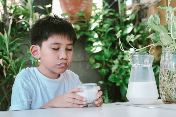 De mond van de jongen was gekleurd met melkvlekken nadat hij de melk uit het glas dronk.. - Foto, afbeelding