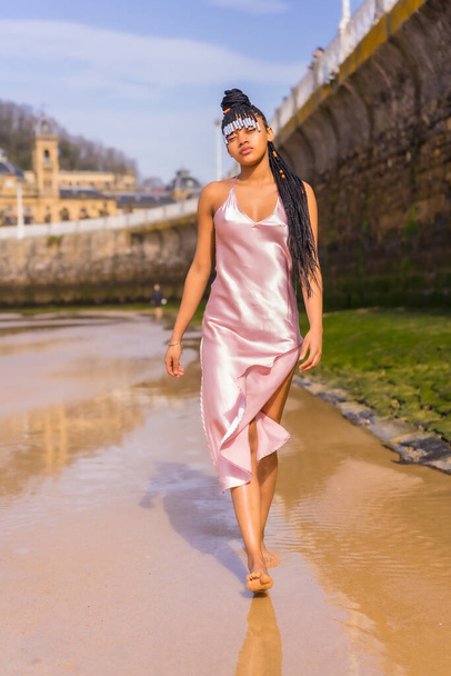 Dominican ethnic girl with braids with a beautiful pink dress. Fashion enjoying the summer walking on the beach - Photo, image