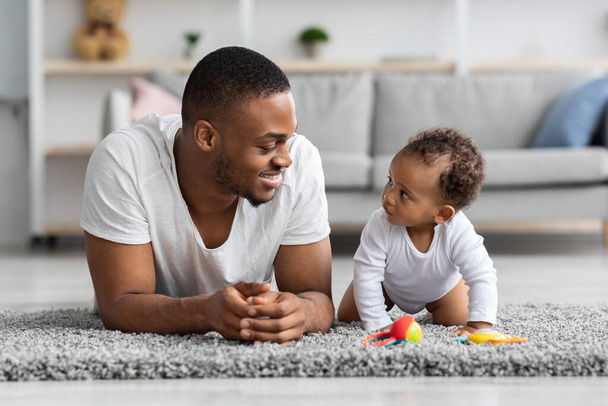 joven negro papá y su adorable bebé relajando juntos en casa - Foto, imagen