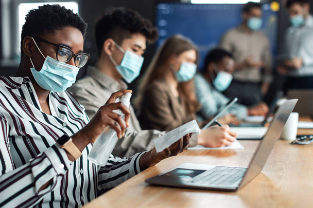 Trabajadores multiculturales con máscaras médicas, mujer negra con desinfectante - Foto, imagen