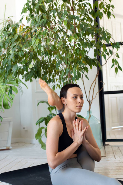 Young beautiful woman is engaged in stretching in a room with plants - 写真・画像