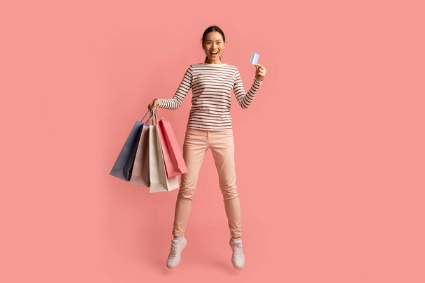 Grandes ventas. Emocionado mujer asiática saltando con bolsas de compras y tarjeta de crédito - Foto, imagen