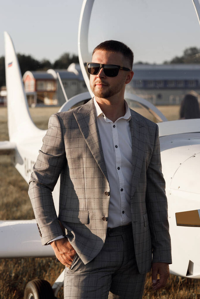 A male pilot, against the background of an airplane at sunset. The groom in a suit is standing near his private plane. - Foto, Bild