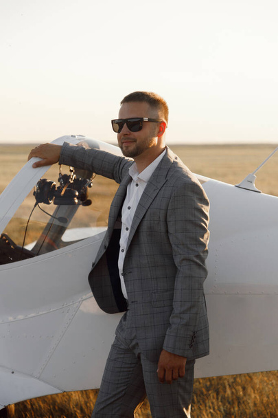 A male pilot, against the background of an airplane at sunset. The groom in a suit is standing near his private plane. - Foto, Imagen