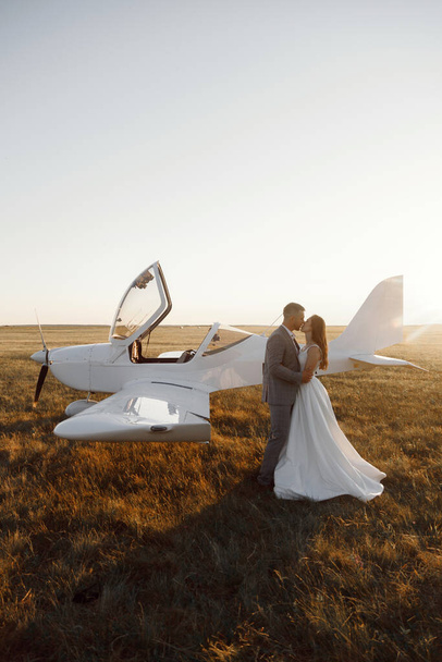 A couple on the background of a private plane at sunset. A sensual wedding couple, the bride and groom are standing together next to the plane. - Photo, image