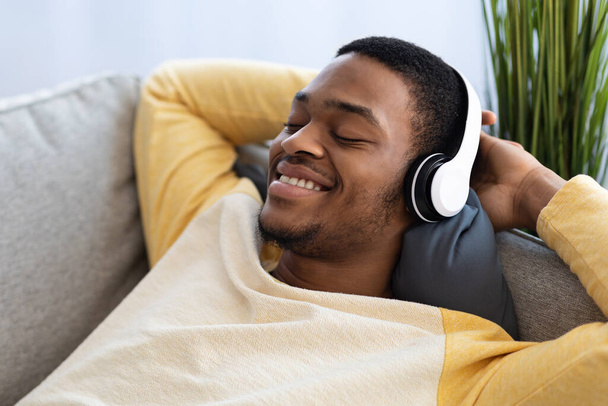 Closeup of relaxed black guy listening to music, using headset - Photo, Image