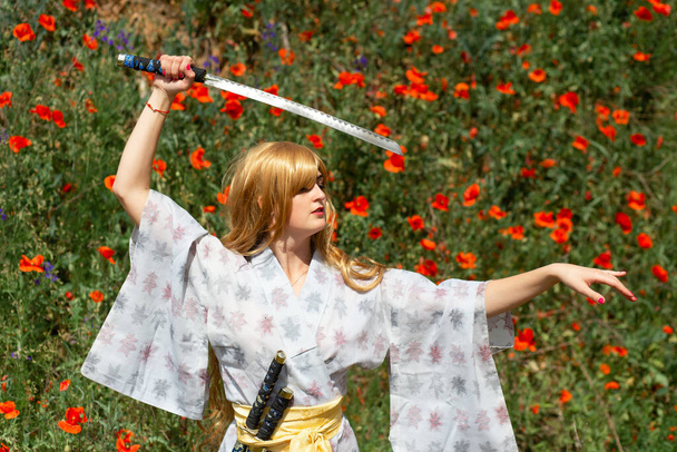Young asian woman in traditional kimono trains fighting techniques with katana sword on the hills with red poppies, samurai warrior girl - Photo, image