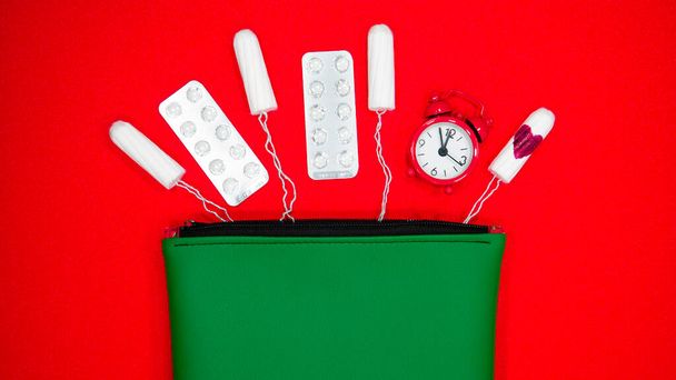Relógio vermelho com tampões e pílulas anticoncepcionais fora do saco cosmético. - Foto, Imagem