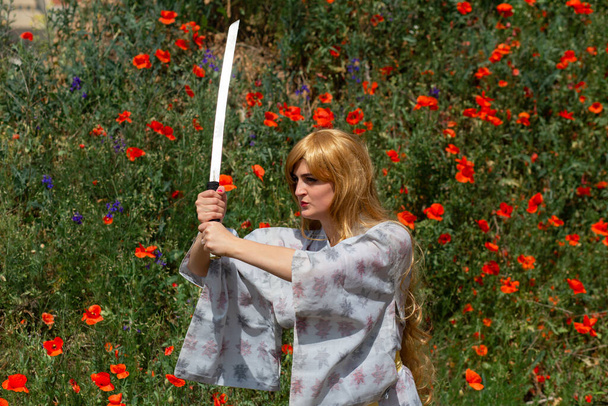 Young asian woman in traditional kimono trains fighting techniques with katana sword on the hills with red poppies, samurai warrior girl - Foto, imagen