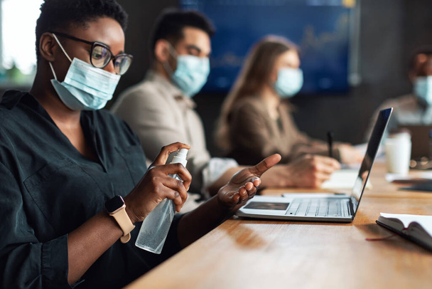 Trabajadores multiculturales con máscaras médicas, mujer negra con desinfectante antibacteriano - Foto, imagen