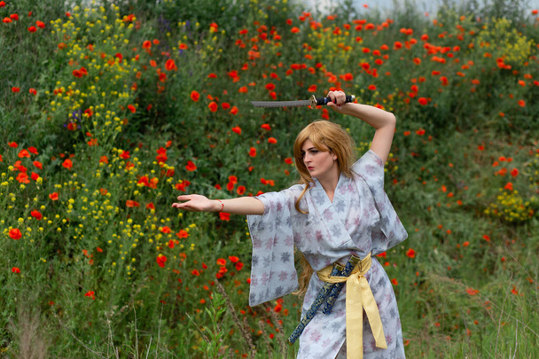 Young asian woman in traditional kimono trains fighting techniques with katana sword on the hills with red poppies, samurai warrior girl - Foto, Imagen