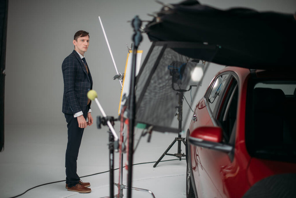Professional male actor works in the frame on the set. Shooting with a car on a large white cyclorama. Handsome young man on the set of a movie, commercial or TV series. Filming indoors, studio - Valokuva, kuva