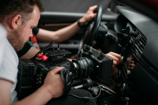 Operatőr egy filmkamerával a forgatáson. Lelőni egy kocsit. Professzionális videós egy film, reklám vagy TV sorozat forgatásán. Filmforgatás zárt térben, stúdió - Fotó, kép